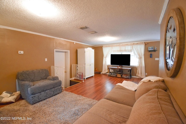 living area with visible vents, ornamental molding, a textured ceiling, and wood finished floors