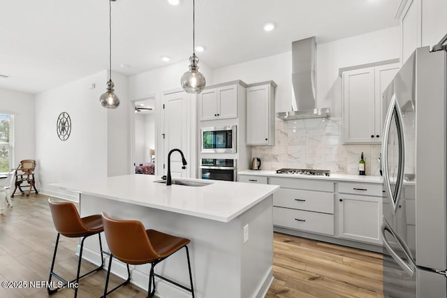 kitchen featuring appliances with stainless steel finishes, a sink, wall chimney exhaust hood, a kitchen bar, and backsplash