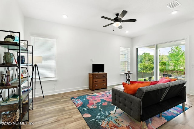 living area with baseboards, a ceiling fan, light wood-style flooring, and visible vents