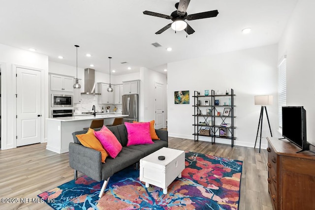 living room featuring ceiling fan, visible vents, baseboards, and light wood finished floors