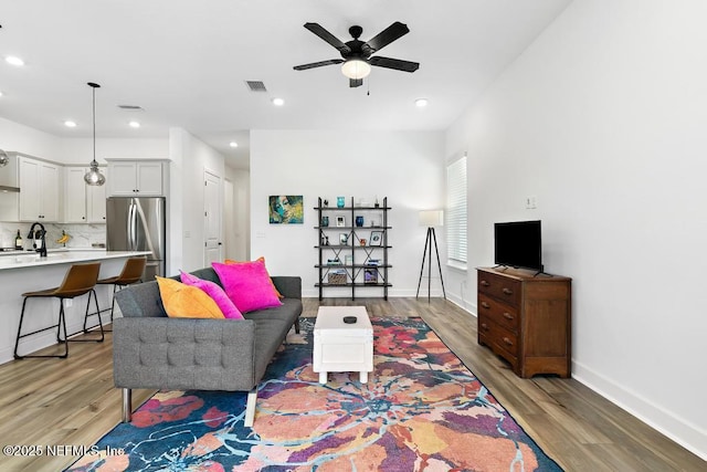 living area featuring light wood-style floors, baseboards, a ceiling fan, and recessed lighting