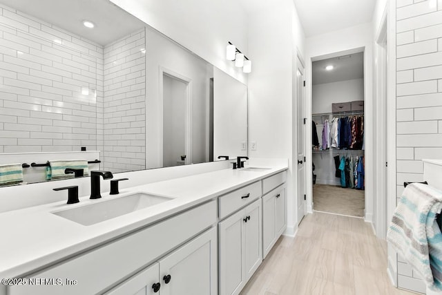 full bathroom featuring double vanity, a walk in closet, a sink, and marble finish floor