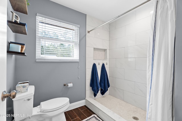 bathroom featuring baseboards, a tile shower, wood finish floors, and toilet