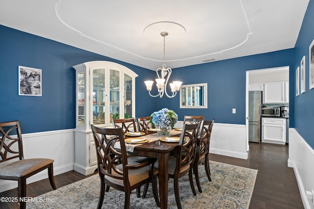 dining area featuring an inviting chandelier, a wainscoted wall, dark wood-style floors, visible vents, and a tray ceiling