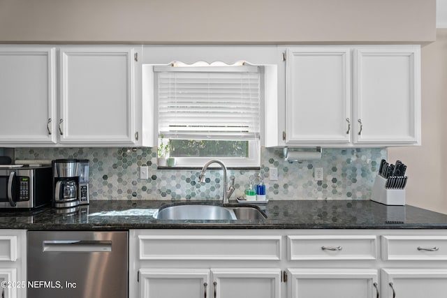 kitchen featuring dark stone counters, a sink, decorative backsplash, white cabinets, and appliances with stainless steel finishes