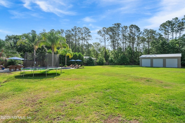 view of yard featuring a detached garage, a trampoline, fence, and an outbuilding