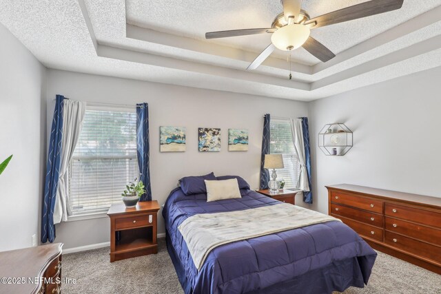 bedroom with a textured ceiling, multiple windows, carpet, and a tray ceiling