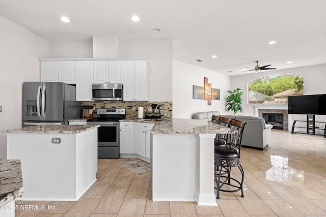 kitchen with a sink, a breakfast bar, ceiling fan, stainless steel appliances, and a peninsula
