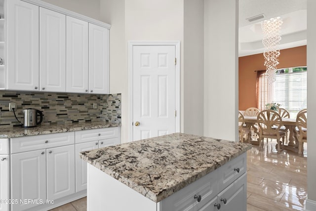 kitchen with a chandelier, light stone countertops, visible vents, and backsplash