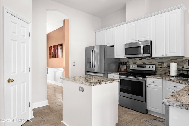 kitchen with decorative backsplash, light stone counters, a kitchen island, white cabinetry, and appliances with stainless steel finishes