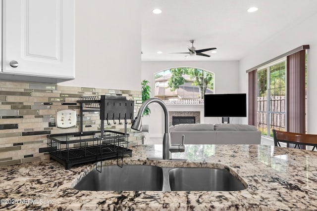 kitchen featuring a sink, ceiling fan, light stone counters, and a healthy amount of sunlight