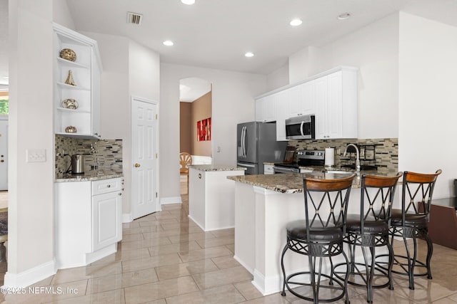 kitchen with open shelves, visible vents, stainless steel appliances, arched walkways, and backsplash