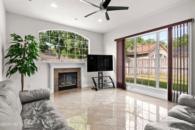 living area featuring recessed lighting, ceiling fan, a glass covered fireplace, marble finish floor, and a textured ceiling