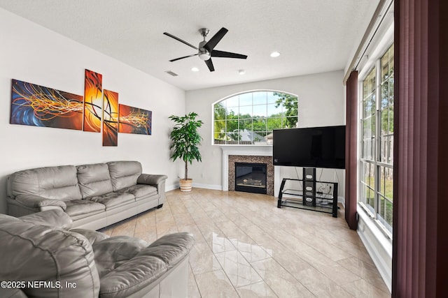 living room with a textured ceiling, visible vents, a glass covered fireplace, recessed lighting, and a ceiling fan