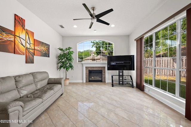 living room featuring a textured ceiling, visible vents, a glass covered fireplace, recessed lighting, and a ceiling fan