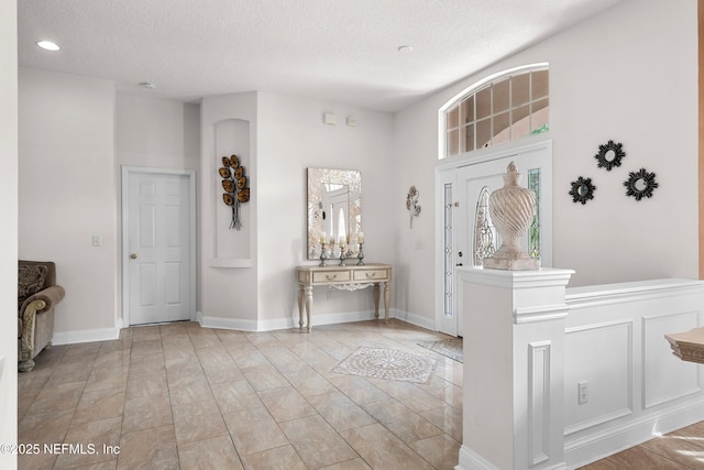 entrance foyer featuring recessed lighting, a textured ceiling, a towering ceiling, and baseboards
