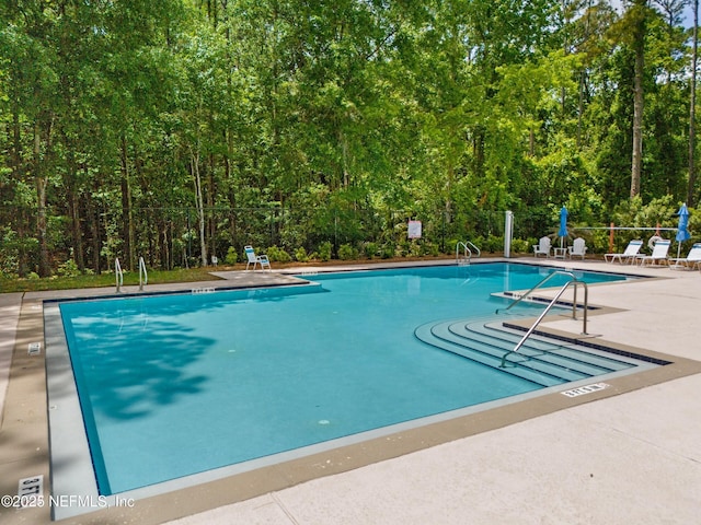 pool featuring a patio, a forest view, and fence