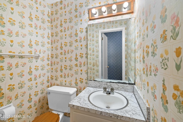 half bathroom with vanity, toilet, and wallpapered walls