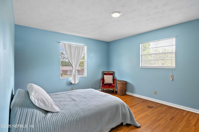 bedroom featuring baseboards, wood finished floors, and multiple windows