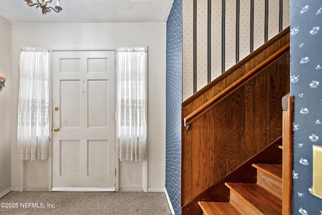 entrance foyer featuring carpet floors, wallpapered walls, baseboards, and stairway