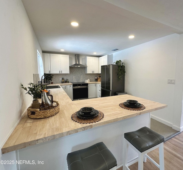 1118 Brookmont Ave E, Jacksonville, FL 32211 - kitchen featuring wall chimney exhaust hood, range, freestanding refrigerator, a breakfast bar area, and a peninsula