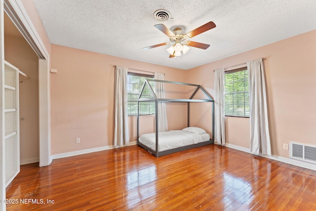 bedroom with baseboards, visible vents, wood finished floors, and a textured ceiling