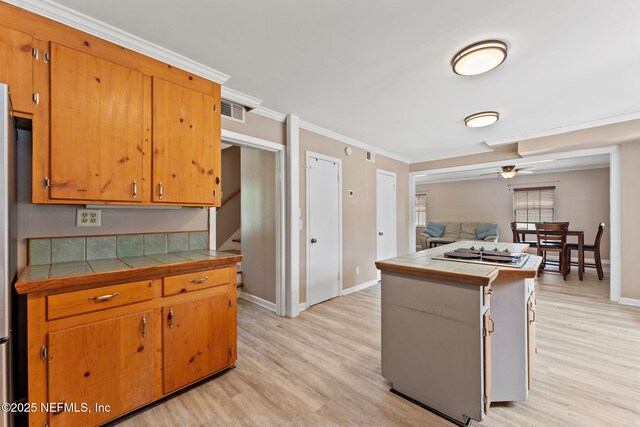 kitchen featuring crown molding, baseboards, tile counters, and light wood-type flooring