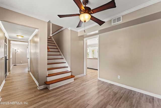 stairs with a ceiling fan, visible vents, baseboards, ornamental molding, and wood finished floors
