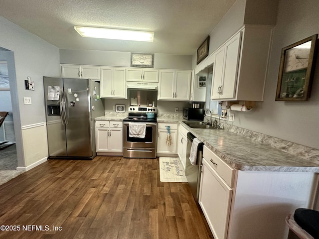 kitchen with a sink, under cabinet range hood, stainless steel appliances, dark wood-type flooring, and white cabinets