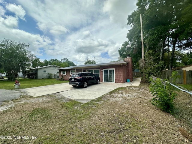 exterior space featuring driveway, a chimney, fence, brick siding, and a front lawn