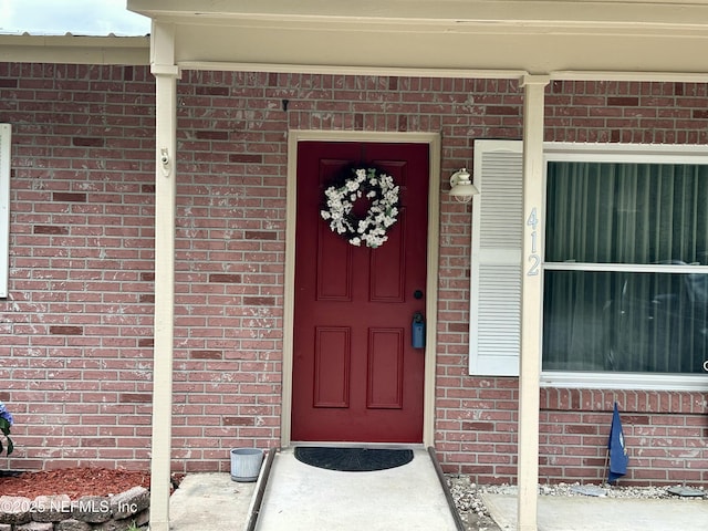 doorway to property featuring covered porch and brick siding