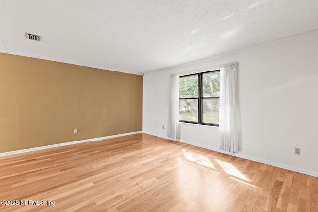 spare room featuring baseboards, light wood-type flooring, a textured ceiling, and visible vents