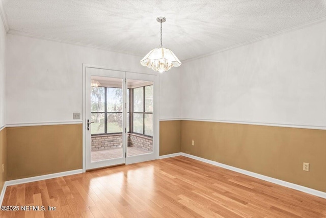 unfurnished room featuring baseboards, a notable chandelier, ornamental molding, and wood finished floors