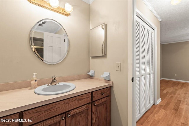 bathroom with crown molding, vanity, a textured ceiling, wood finished floors, and visible vents