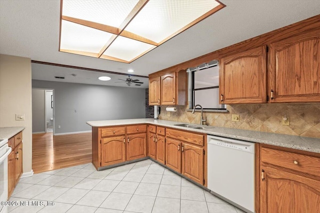 kitchen featuring brown cabinetry, white dishwasher, a sink, and decorative backsplash