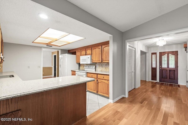 kitchen with light countertops, a sink, a peninsula, white appliances, and light wood-style flooring
