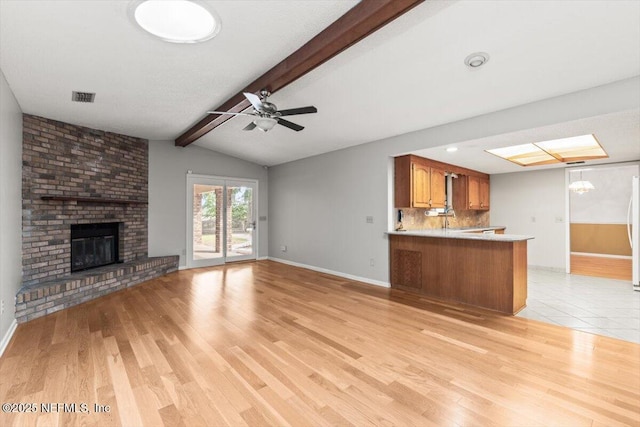 unfurnished living room with baseboards, lofted ceiling with beams, a brick fireplace, and light wood finished floors