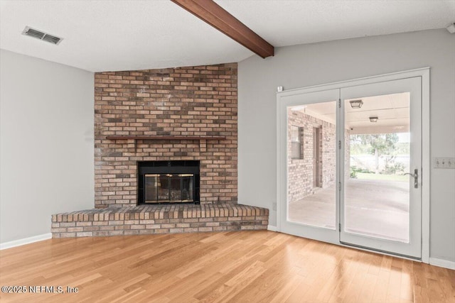 unfurnished living room featuring visible vents, a fireplace, wood finished floors, baseboards, and vaulted ceiling with beams