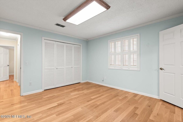 unfurnished bedroom featuring crown molding, a closet, light wood-type flooring, and visible vents