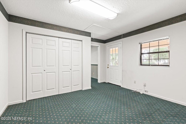 unfurnished bedroom featuring attic access, a textured ceiling, baseboards, a closet, and dark carpet