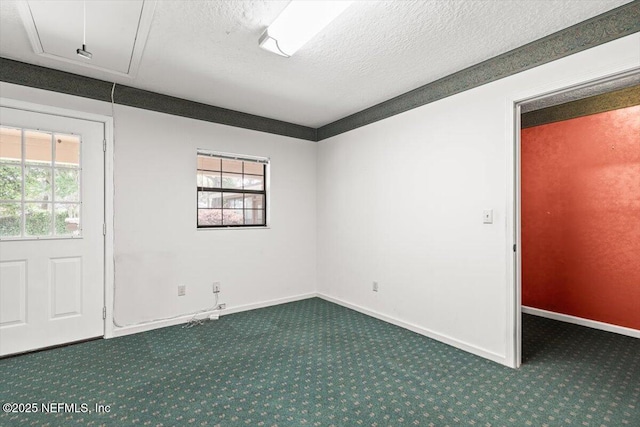 carpeted empty room with a textured ceiling, baseboards, and attic access