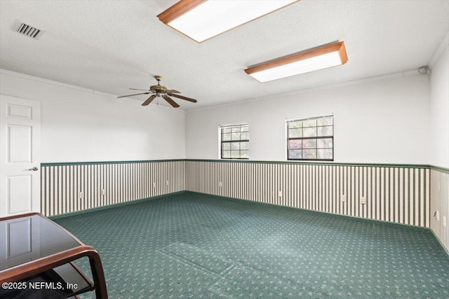 empty room featuring carpet floors, a ceiling fan, visible vents, and ornamental molding