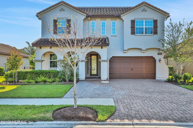 mediterranean / spanish-style home featuring a tile roof, decorative driveway, a front yard, stucco siding, and a garage