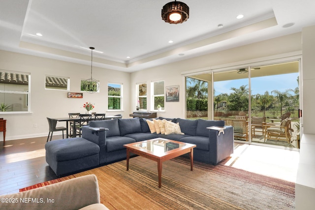 living area with recessed lighting, wood finished floors, a raised ceiling, and plenty of natural light