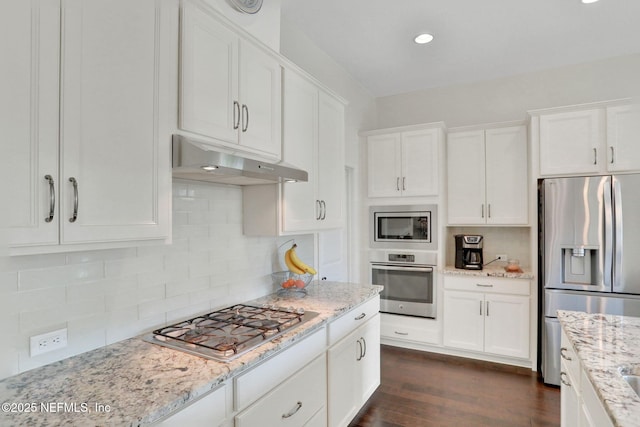 kitchen with white cabinetry, appliances with stainless steel finishes, under cabinet range hood, light stone countertops, and dark wood finished floors