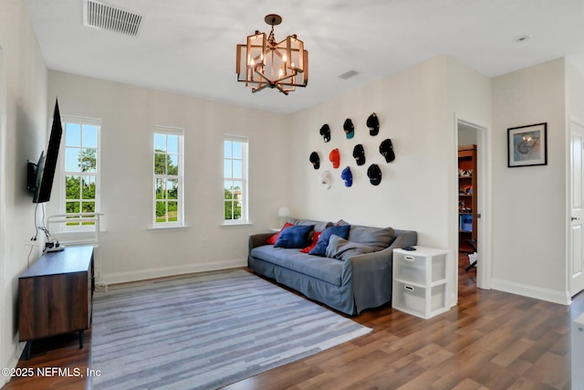 living room with an inviting chandelier, visible vents, wood finished floors, and baseboards
