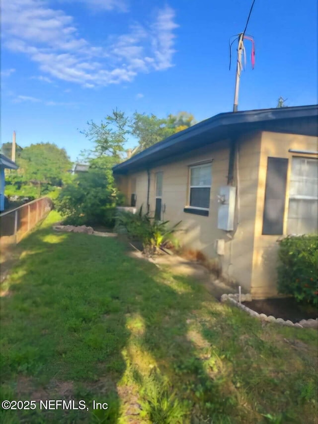 view of side of home with fence, concrete block siding, and a yard