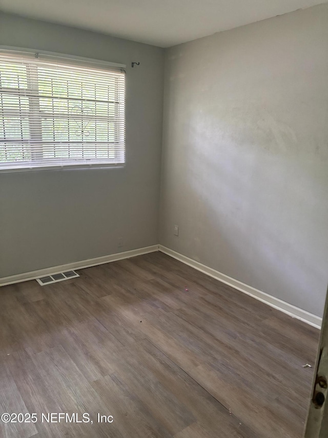 empty room featuring wood finished floors, visible vents, and baseboards