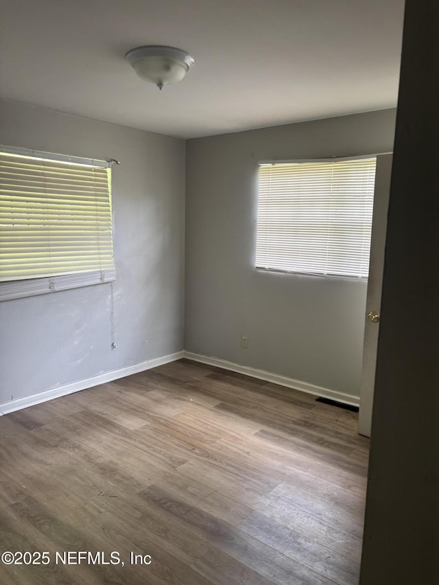 spare room with baseboards, wood finished floors, and a healthy amount of sunlight