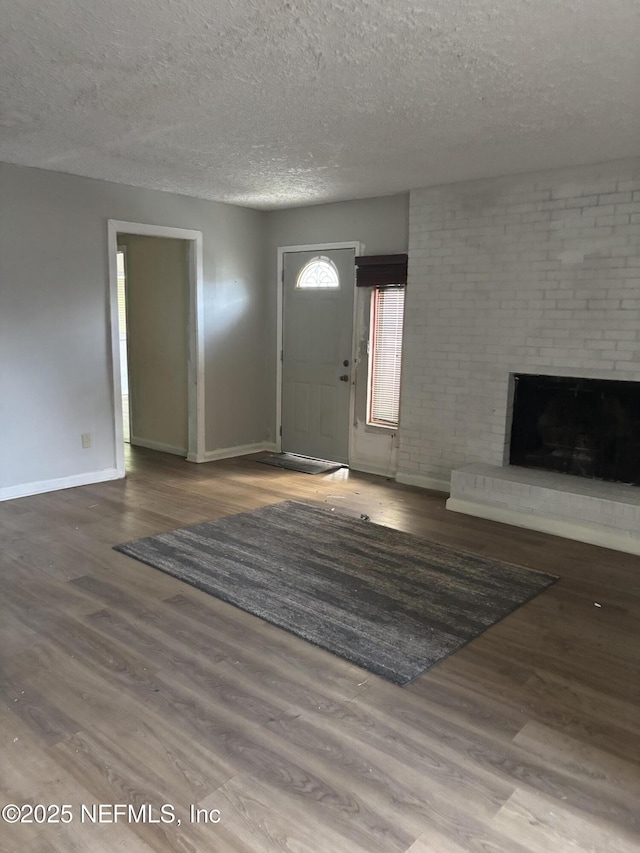 entryway featuring a fireplace, a textured ceiling, wood finished floors, and baseboards